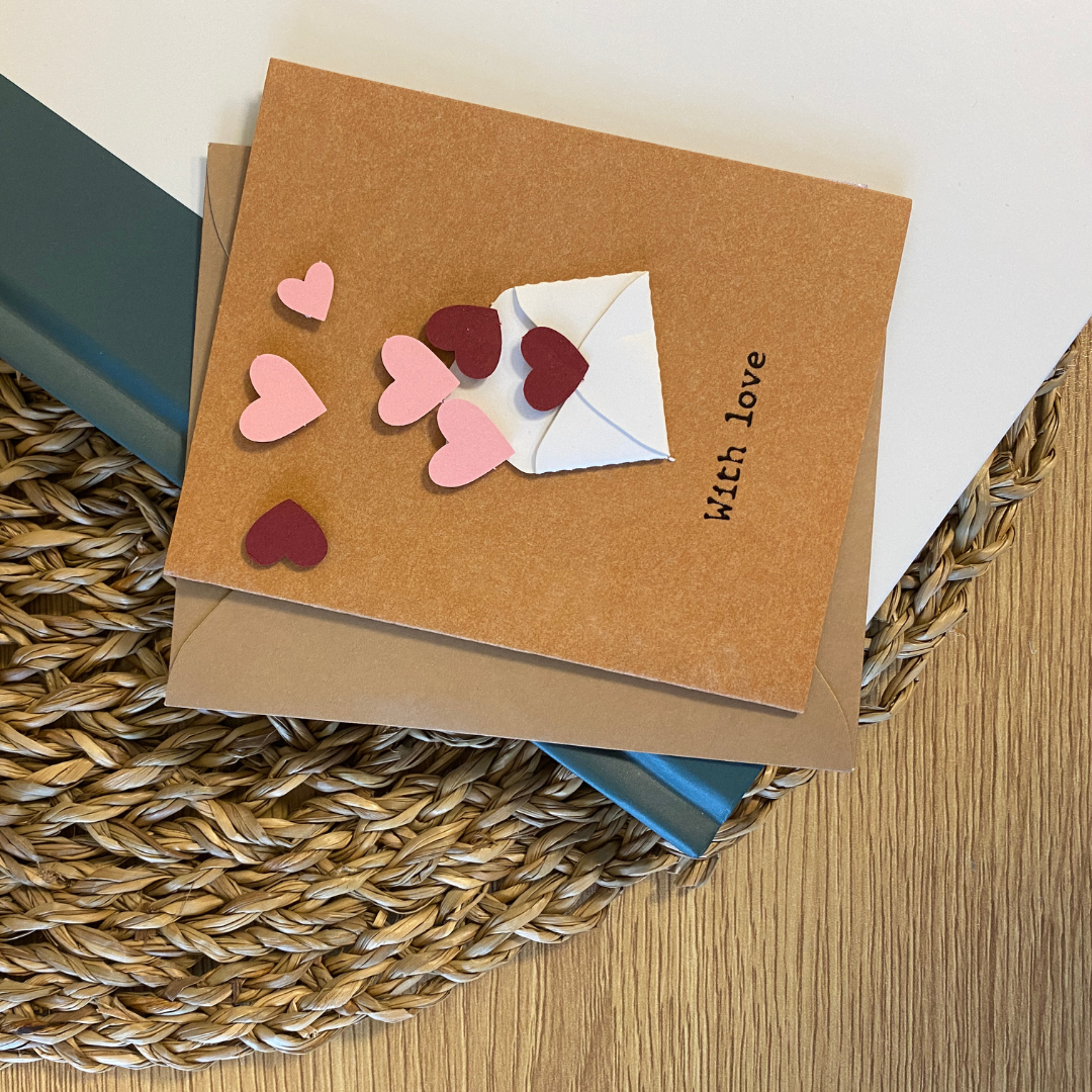 Carte de souhaits en papier kraft avec enveloppe blanche d'où sortent des coeurs rouges et roses.